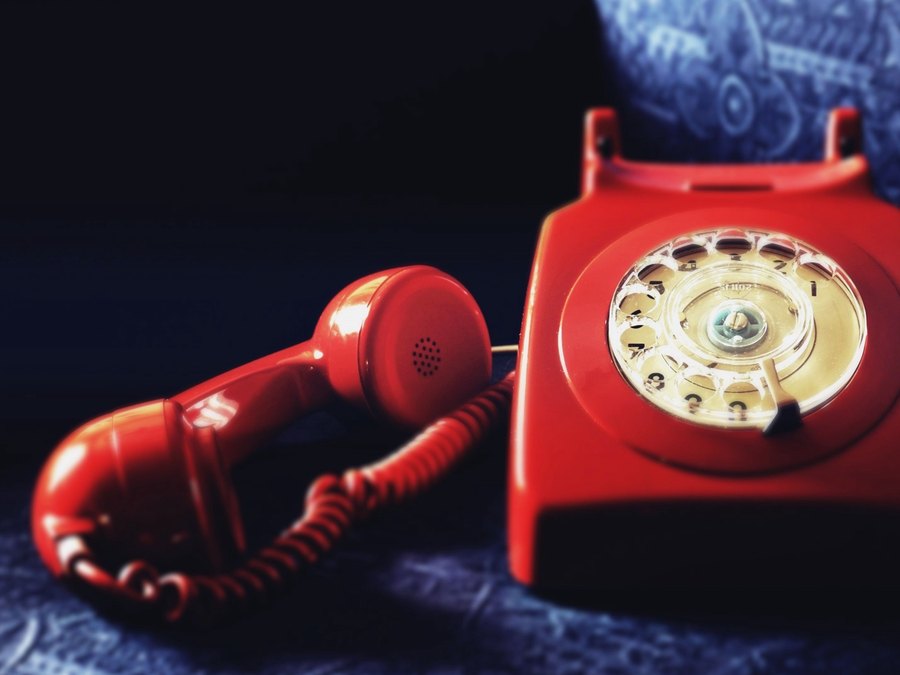 Een rode telefoon met kiesschijf, de hoorn naast het toestel